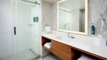 Un baño moderno con cabina de ducha de vidrio, un espejo grande y un lavabo con almacenamiento.