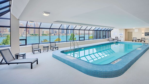 An indoor swimming pool with a city view, lounge chairs, and a tiled deck.