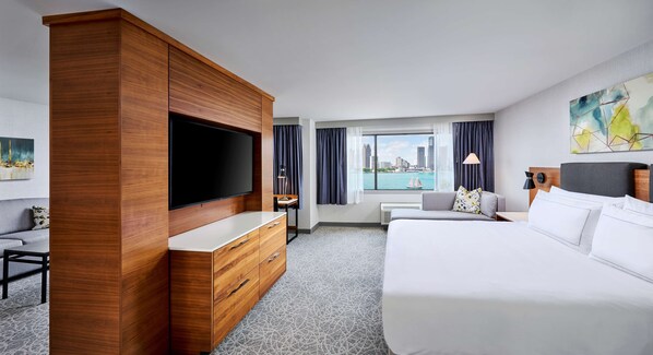 Habitación de hotel con una cama grande, un armario de madera, un televisor de pantalla plana, un escritorio con silla y vistas a la ciudad por la ventana.