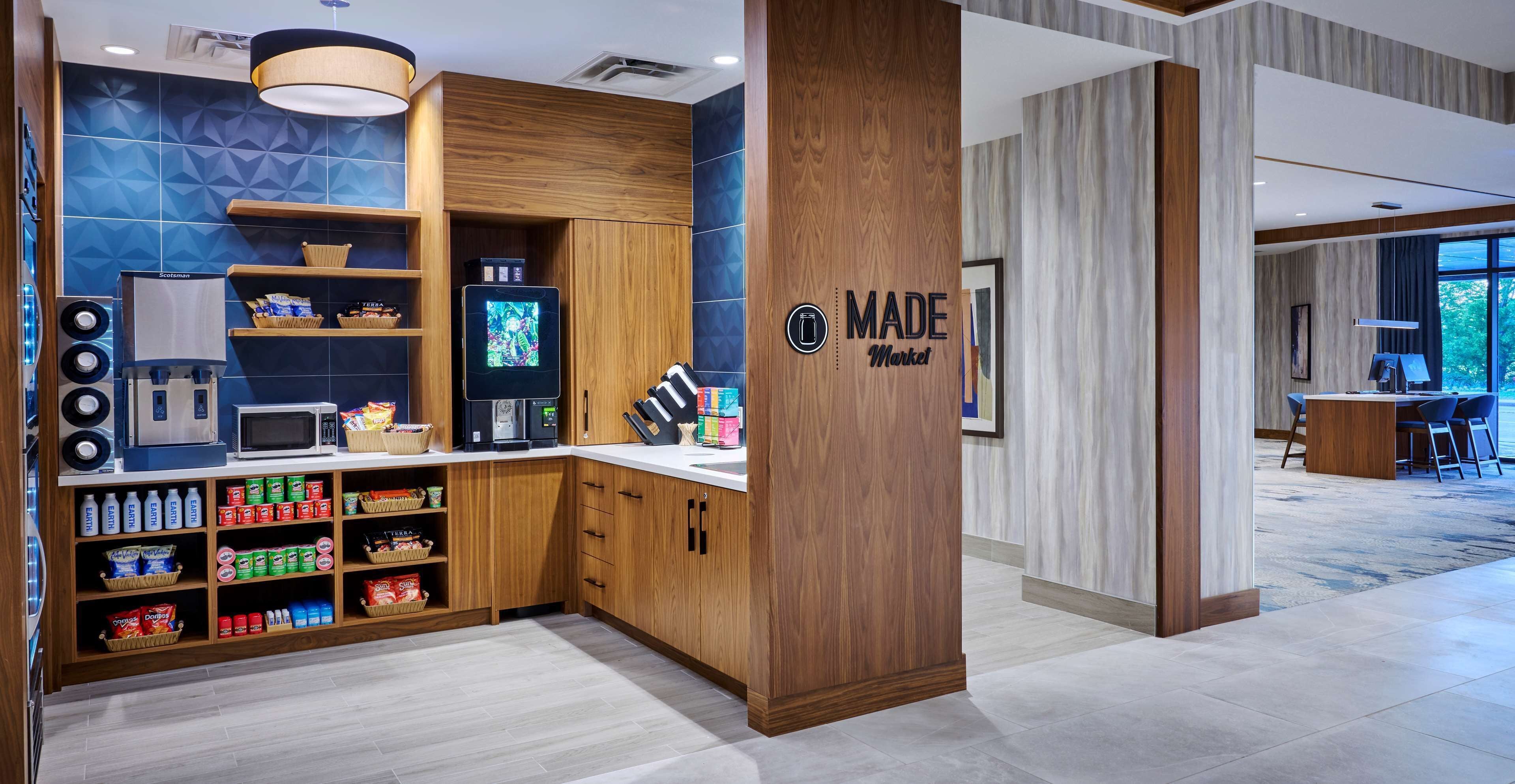 A modern kitchen area with a microwave, toaster, and coffee machine. There are shelves with snacks and beverages. A sign reads "MADE Market."
