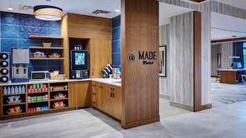 A modern kitchen area with a microwave, toaster, and coffee machine. There are shelves with snacks and beverages. A sign reads "MADE Market."