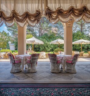 An outdoor patio with tables and chairs, surrounded by greenery and trees.