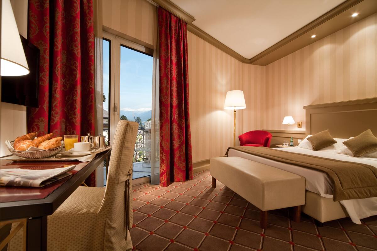 Une chambre d’hôtel comprenant un lit, un bureau avec un petit-déjeuner, une chaise, une lampe et une vue sur l’extérieur.