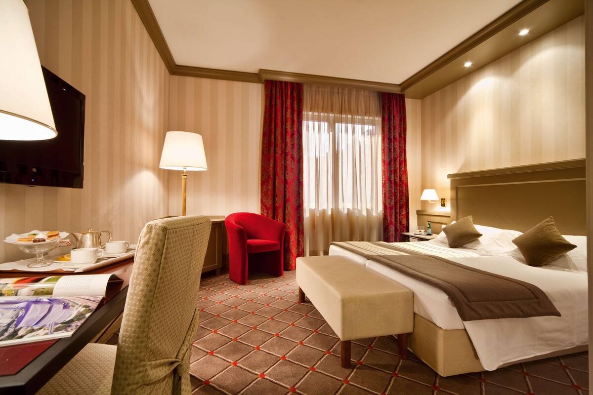 Une chambre d’hôtel comprenant un lit, un bureau avec une lampe, une chaise, une table de chevet et un téléviseur.