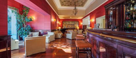 A bar area with wooden flooring, bar stools, and a bar counter with a variety of bottles.