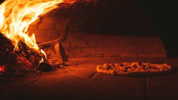 Forno a pizza com parede de tijolos e fogo aceso no interior.