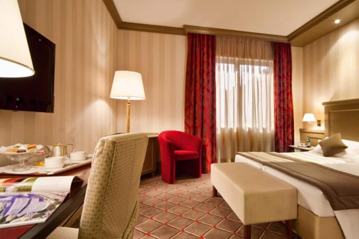 Hotellihuone, jossa on sänky, työpöytä, tuoli, pieni lamppupöytä ja televisio.