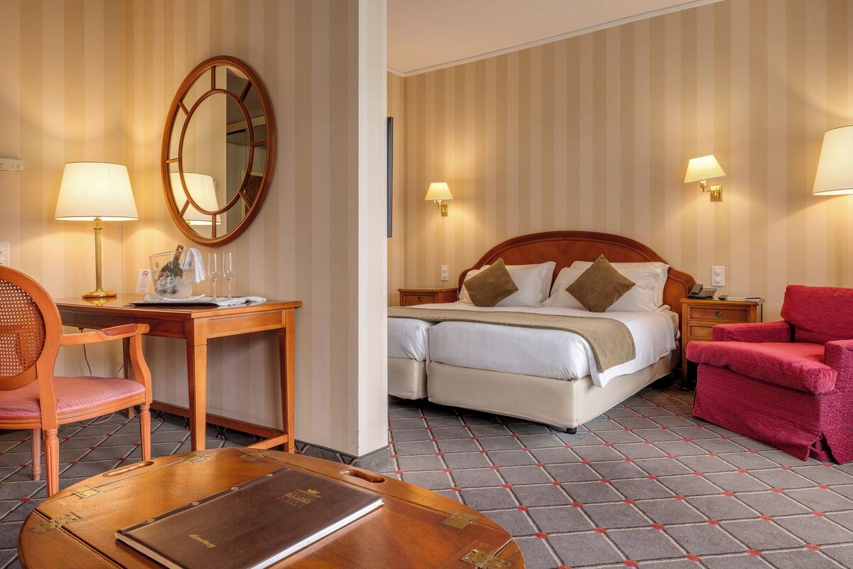Une chambre d’hôtel avec un lit, un bureau et une chaise, un fauteuil rouge et une table en bois.