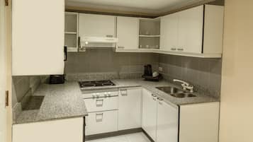 Una cocina compacta con gabinetes blancos, estufa integrada, lavamanos y cafetera.
