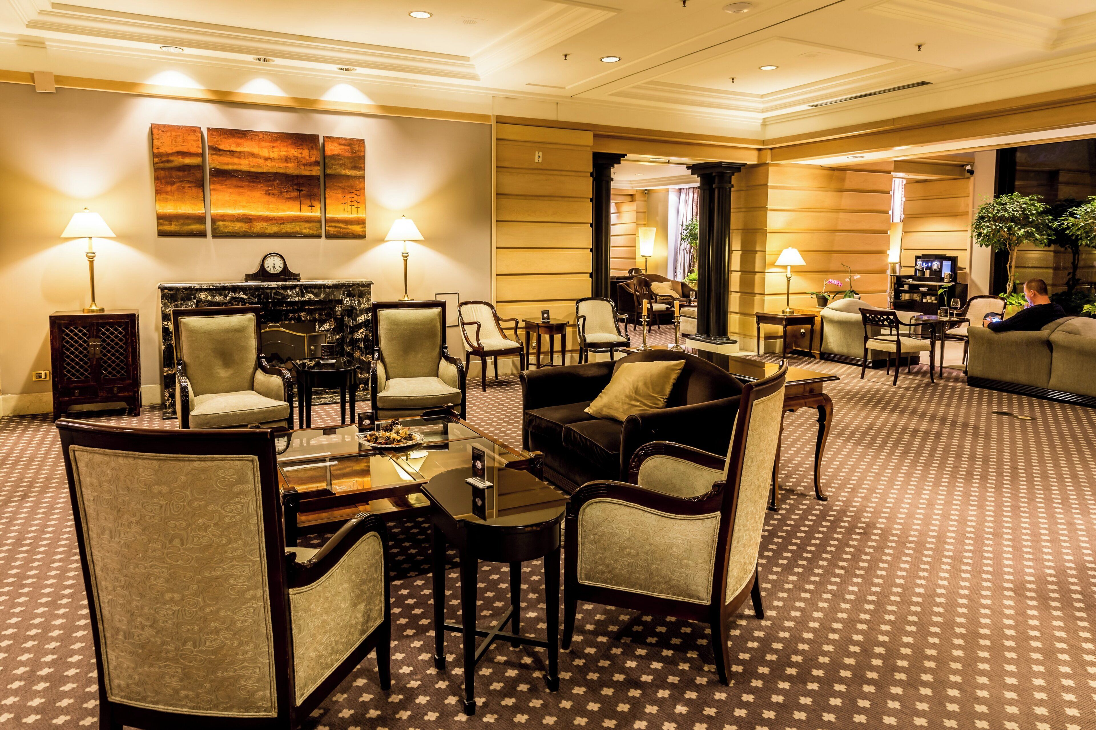 A hotel lobby with a central seating area, multiple armchairs, a coffee table, and a television.