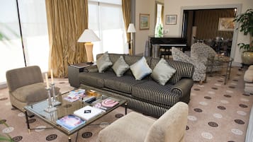 A living room with a sofa, armchairs, a coffee table, a piano, and a dining area.