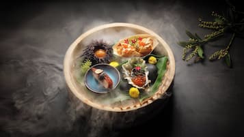 A wooden bowl with various food items, including a fish, a shell with roe, and some green leaves.