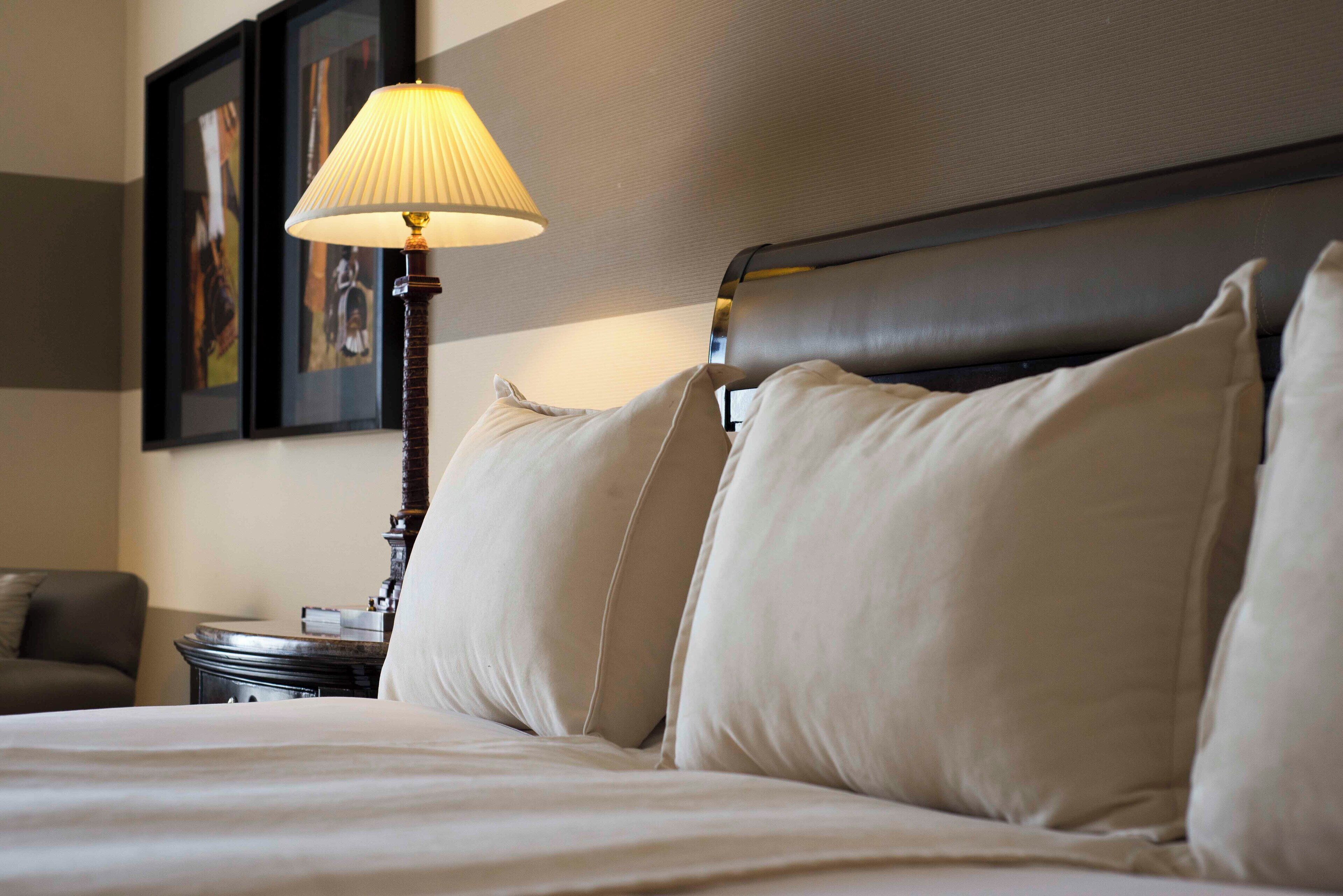 A neatly made bed with a headboard, a bedside lamp, and a framed picture on the wall.