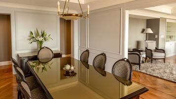 A dining area with a glass table, six chairs, a chandelier, and a vase with flowers.