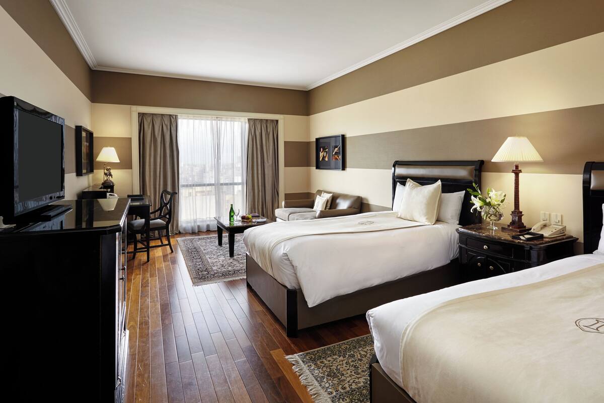 A hotel room with two beds, a desk, a TV, and a window with curtains.