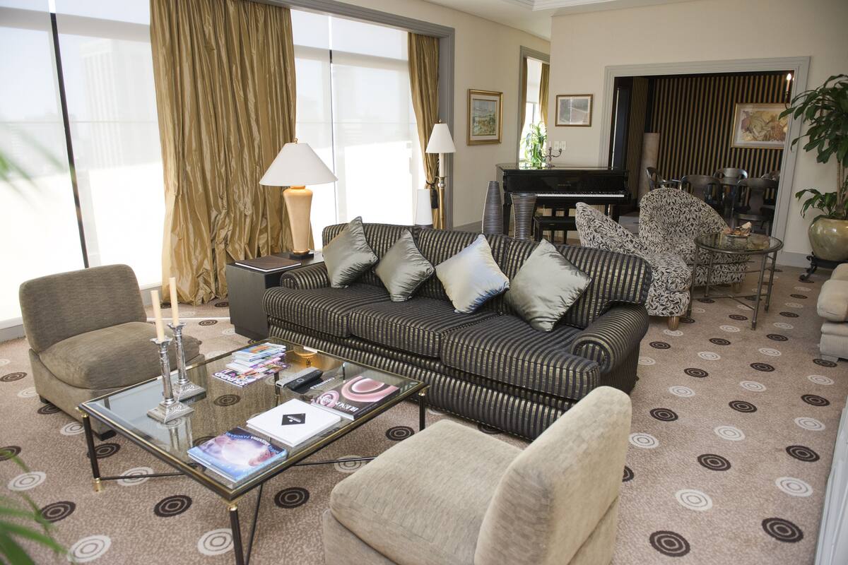 A living room with a sofa, armchairs, a glass coffee table, a piano, and a dining area.
