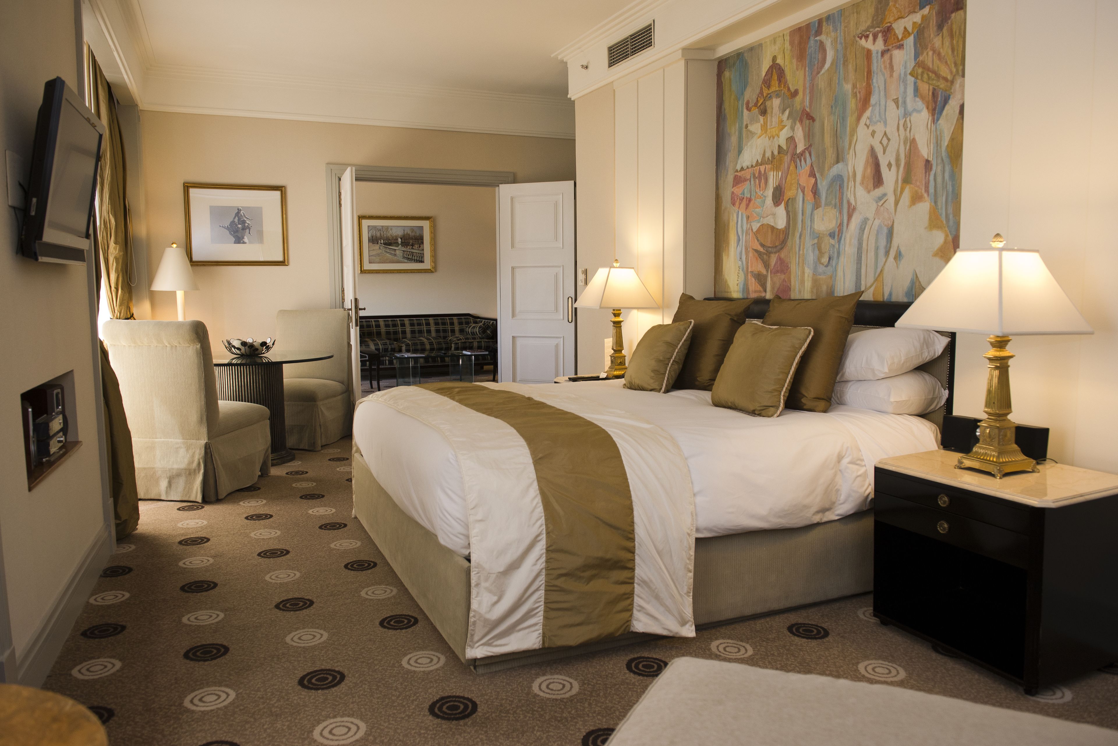 Een hotelkamer met een groot bed, twee nachtkastjes met lampen, een stoel, een bijzettafeltje en een schilderij aan de muur.