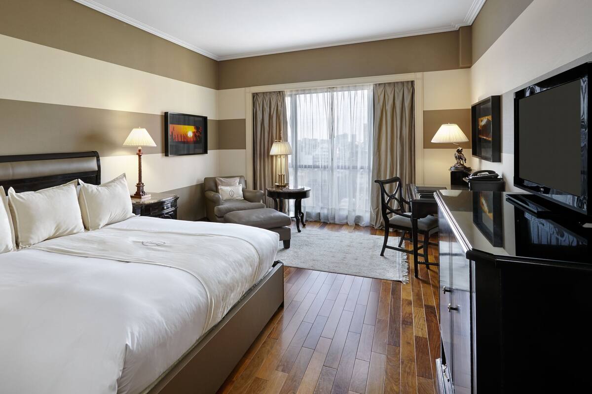 A hotel room with a large bed, a desk with a chair, a television, and a window with curtains.