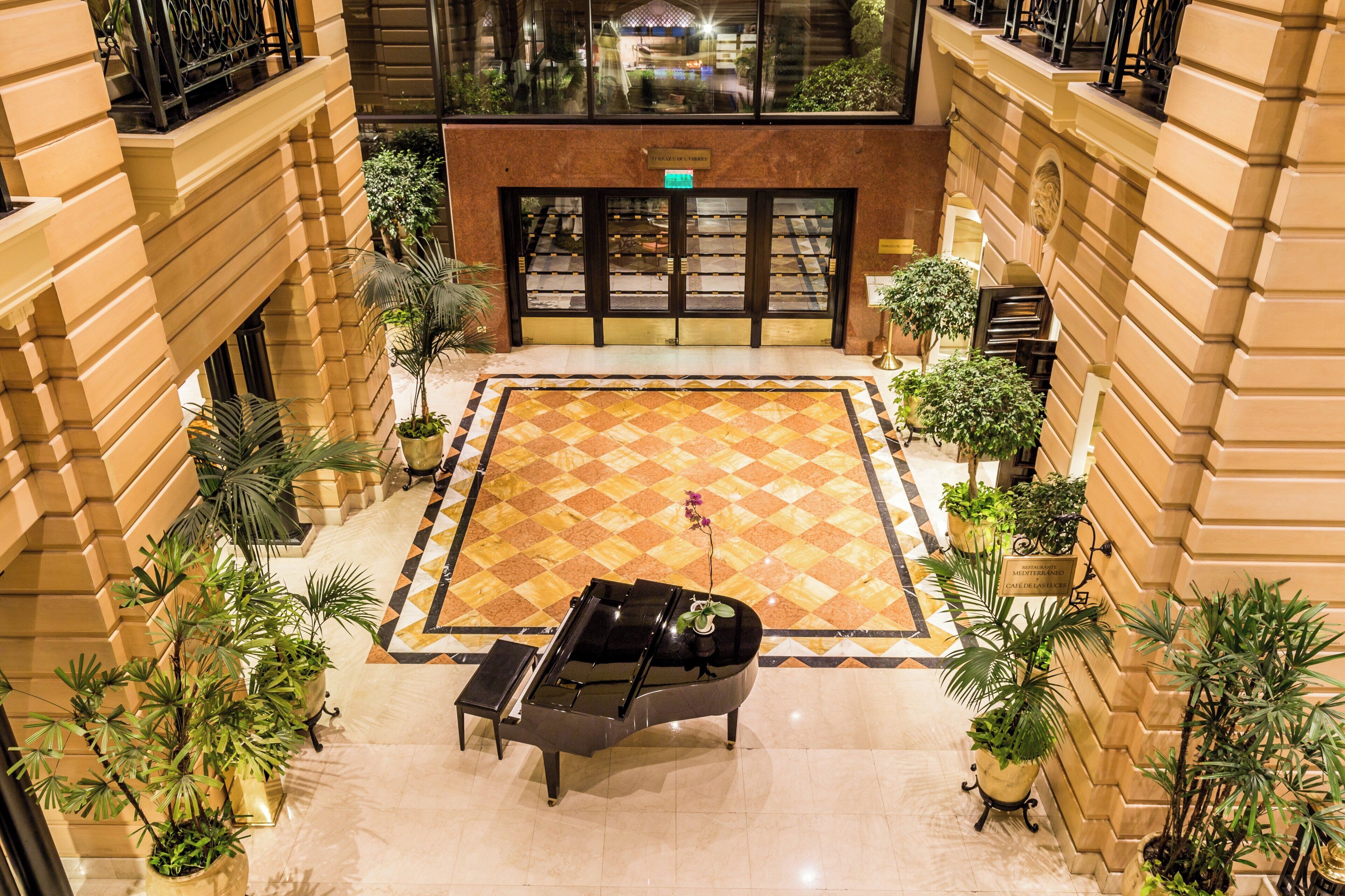 Un hall de hotel con piso a cuadros, un piano y plantas en macetas.