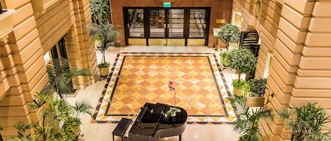 A hotel lobby with a checkered floor, a piano, and potted plants.