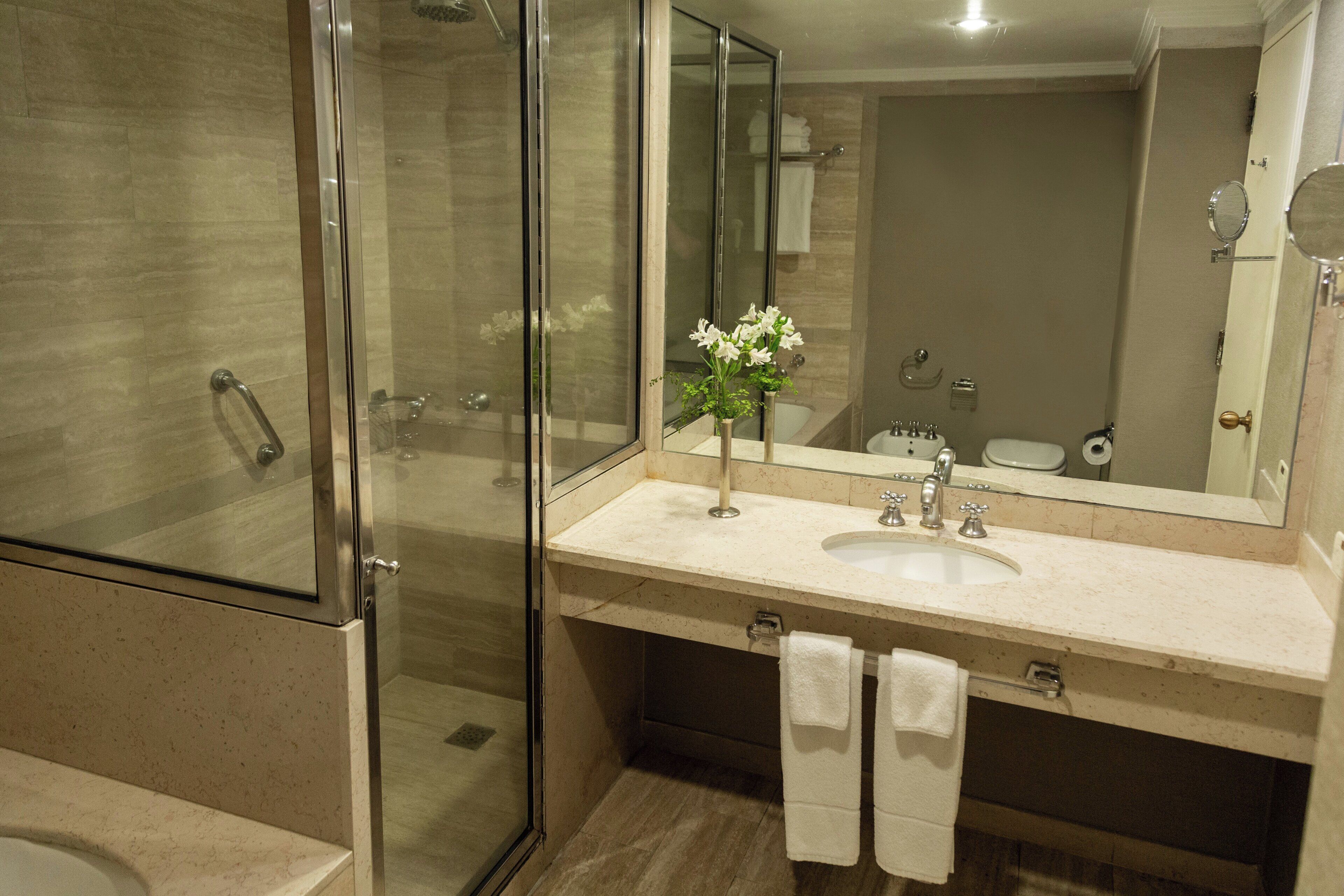 A modern bathroom with a glass-enclosed shower, a sink with a mirror, and a vase with flowers.