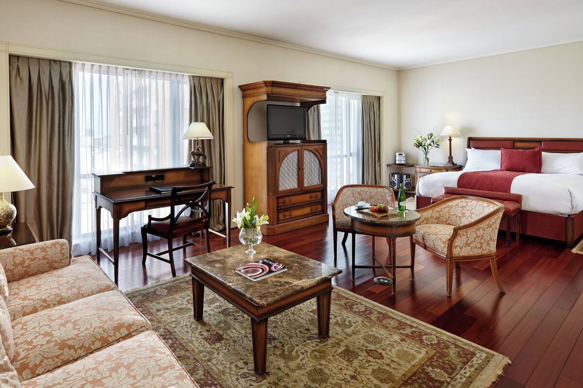 A hotel room with a living area, a dining table, a sofa, a bed, and a TV.