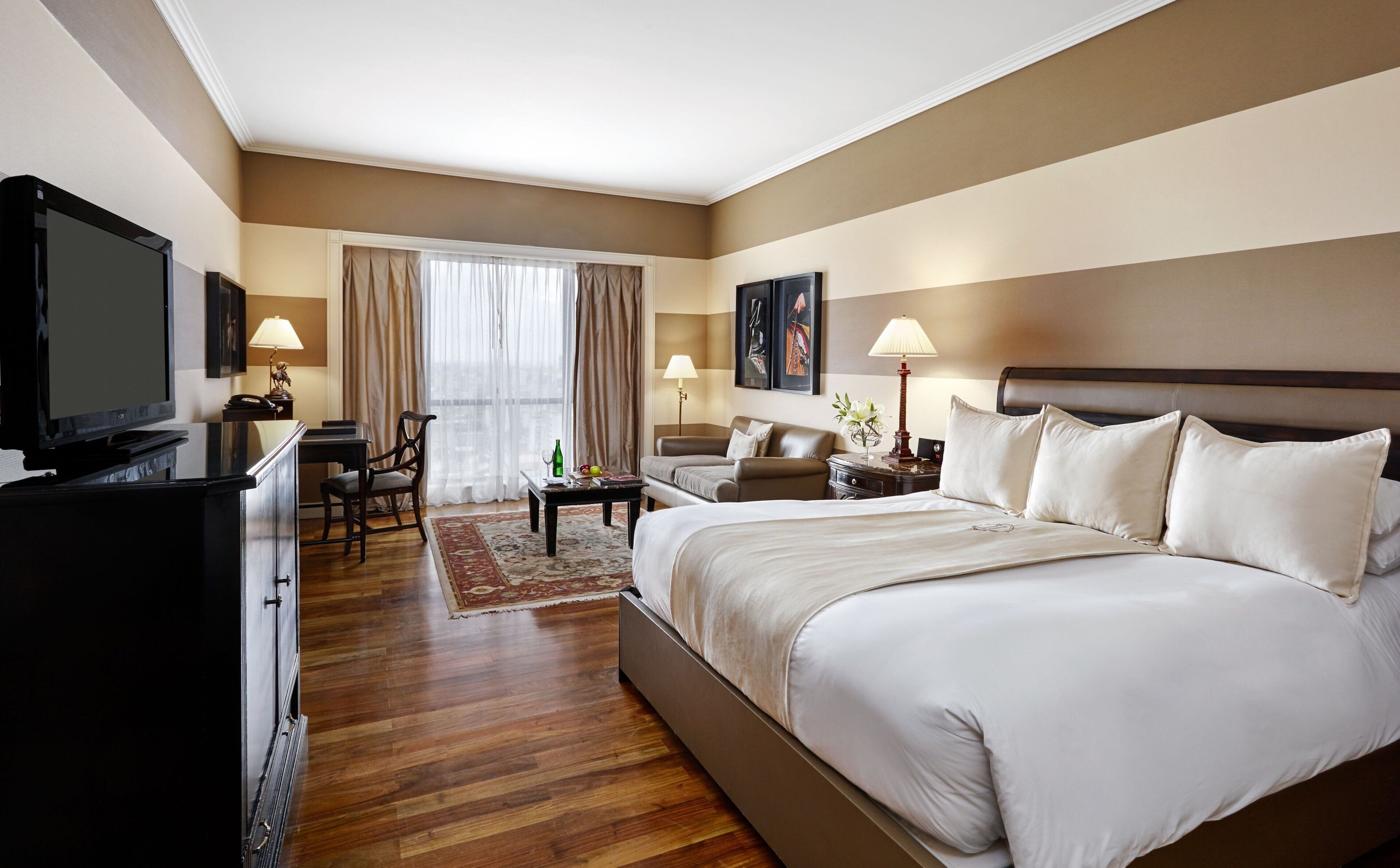 A hotel room with a large bed, a desk, a television, and a window with curtains.