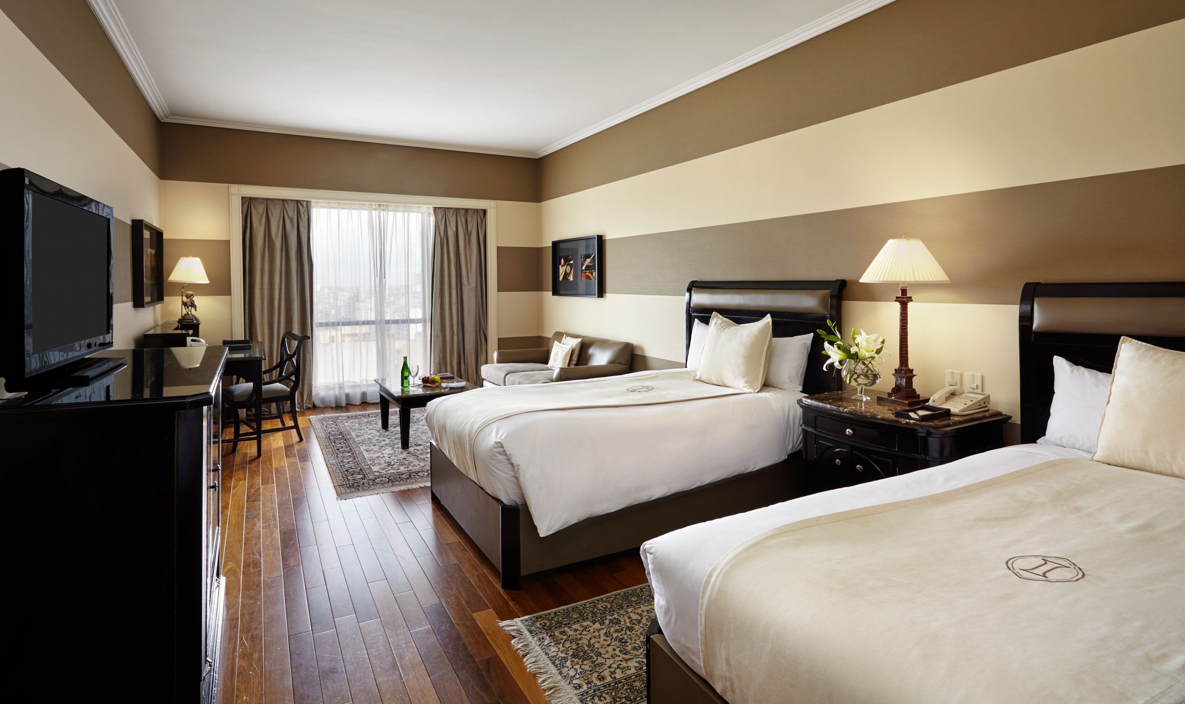 A hotel room with two beds, a desk, a television, and a window with curtains.