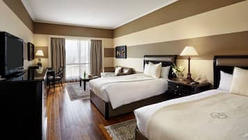 A hotel room with two beds, a desk, a television, and a window with curtains.