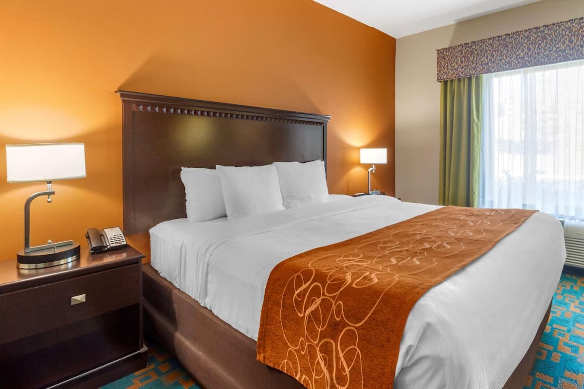 Une chambre d’hôtel avec un grand lit, deux tables de chevet avec des lampes, un téléphone et une fenêtre avec des rideaux.