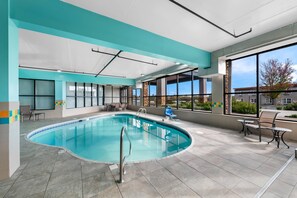 An indoor swimming pool with clear glass walls, a tiled floor, and a seating area with chairs and tables. - Comfort Suites Knoxville West - Farragut (Knoxville)