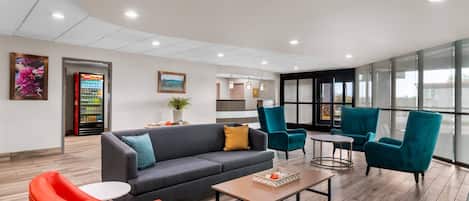 A modern lobby with a grey sofa, red and teal chairs, a coffee table, and a vending machine.