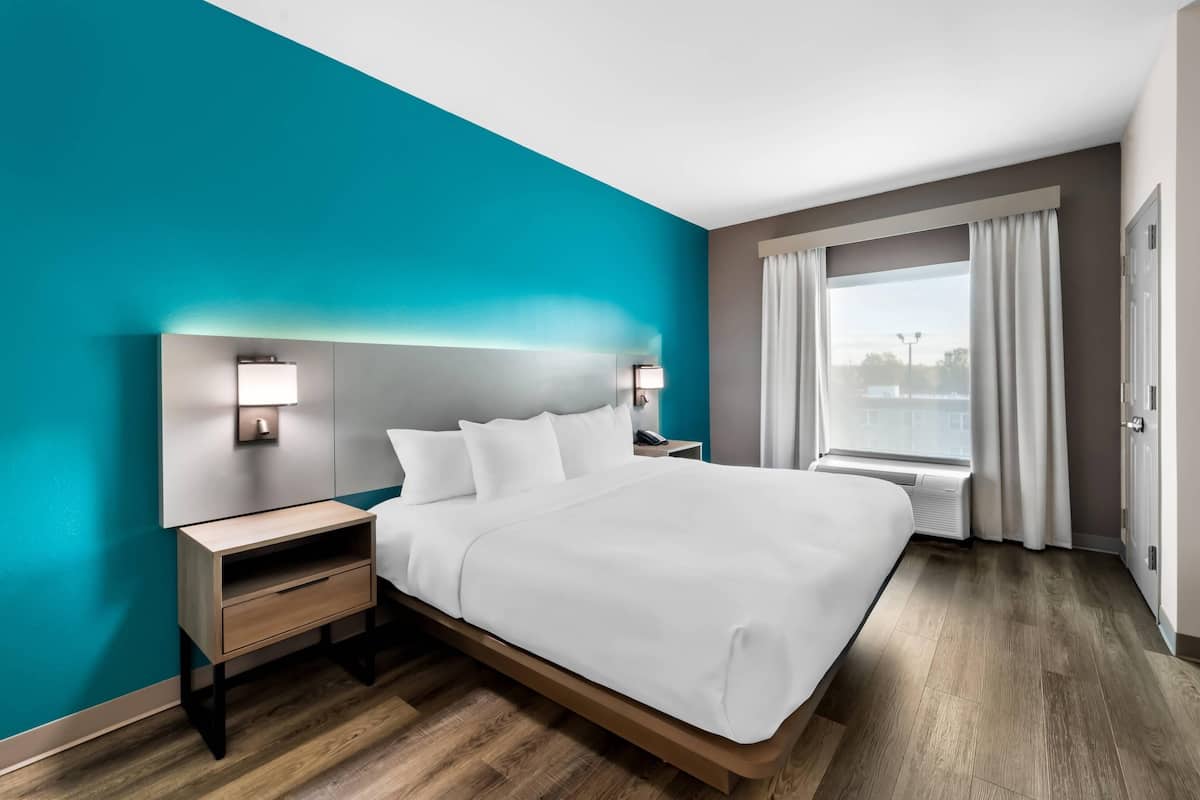 Une chambre d’hôtel moderne avec un grand lit, une table de chevet, une lampe fixée au mur et une fenêtre avec des rideaux.
