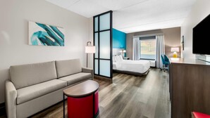 Una habitación de hotel moderna con sofá, una mesita auxiliar roja, cama, escritorio y televisor.