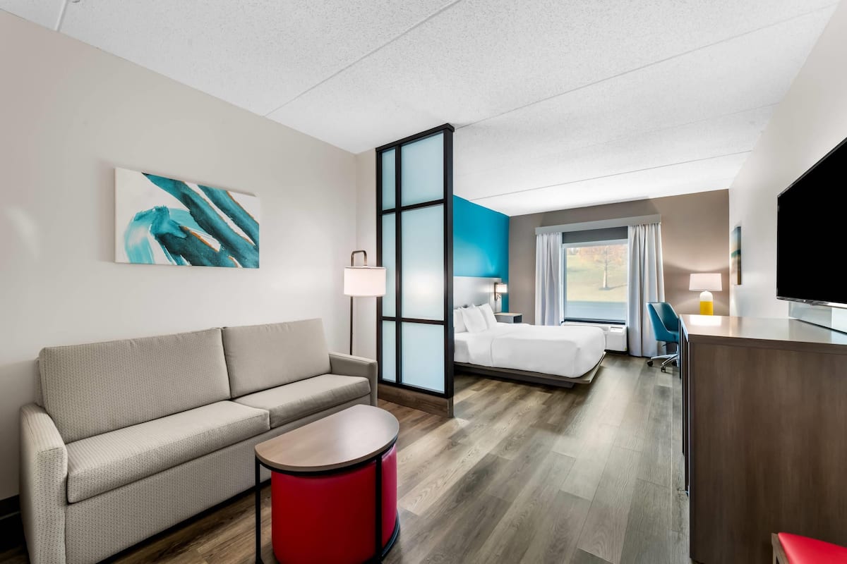 Une chambre d’hôtel moderne avec un canapé, une table de chevet rouge, un lit, un bureau et un téléviseur.