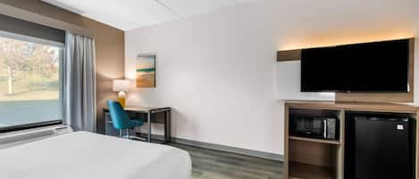 A hotel room with a large bed, a desk with a chair, a flat-screen TV, a microwave, and a refrigerator.