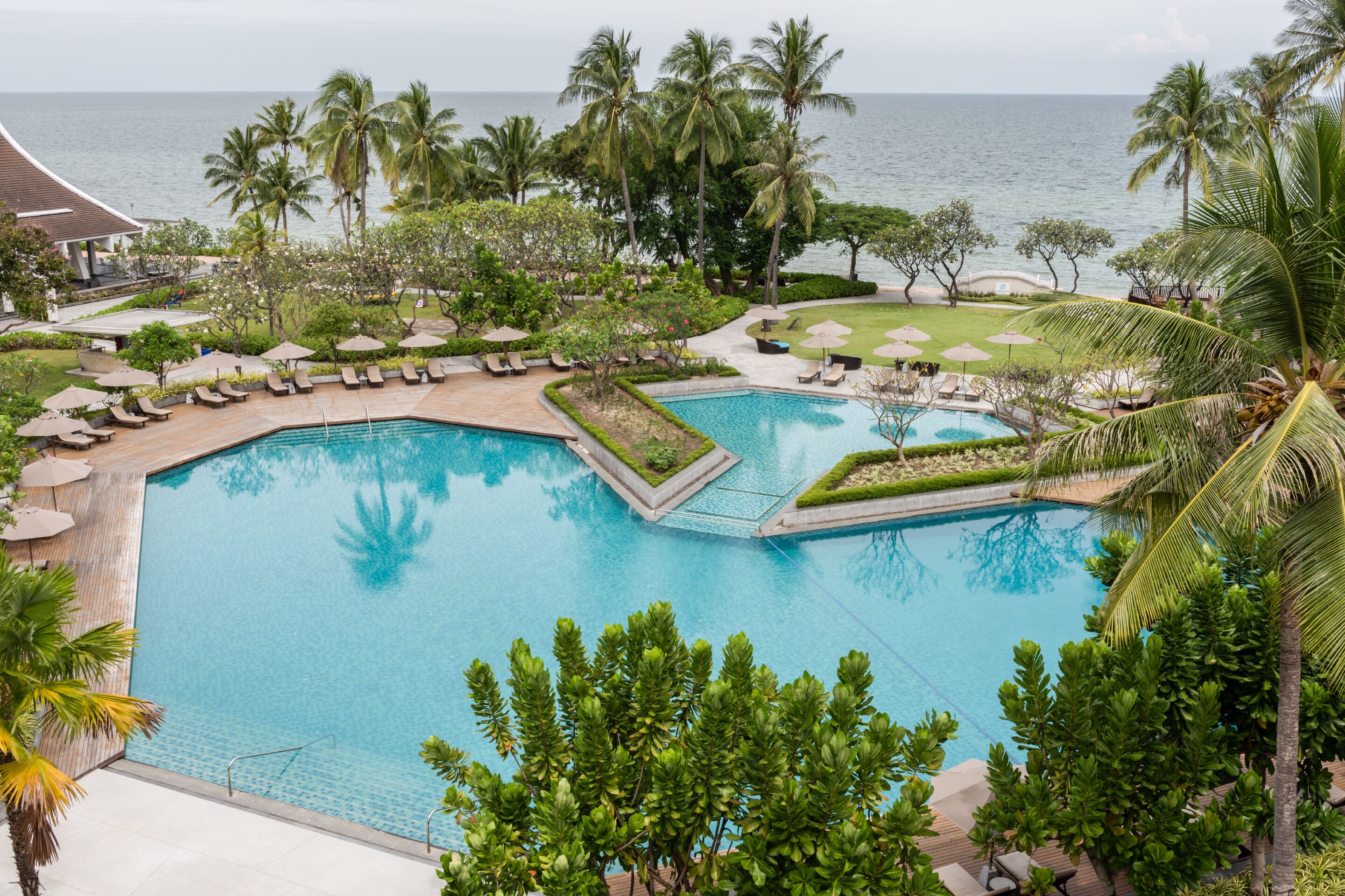 A large pool with a surrounding deck, palm trees, and a view of the ocean.