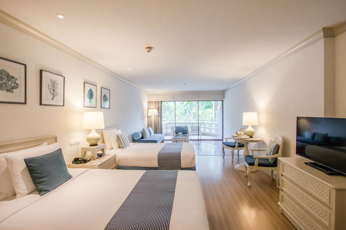 A hotel room with two beds, a TV, a balcony with seating, and artwork on the walls.