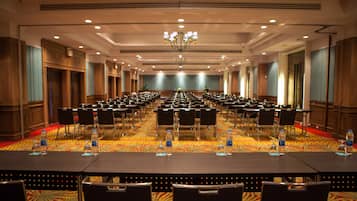 A large conference room with rows of tables and chairs, equipped with water bottles and nameplates.