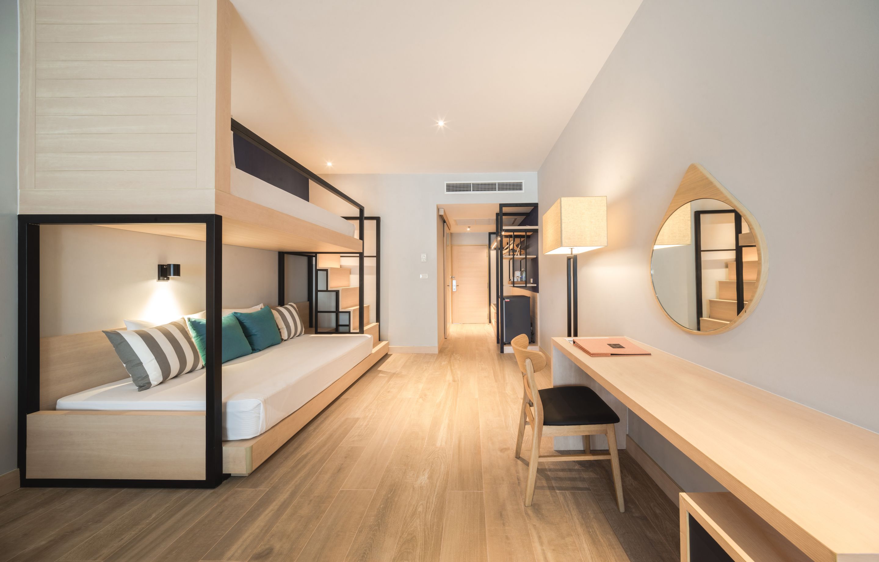 A modern hotel room with a bunk bed, a desk, a chair, and a large mirror.