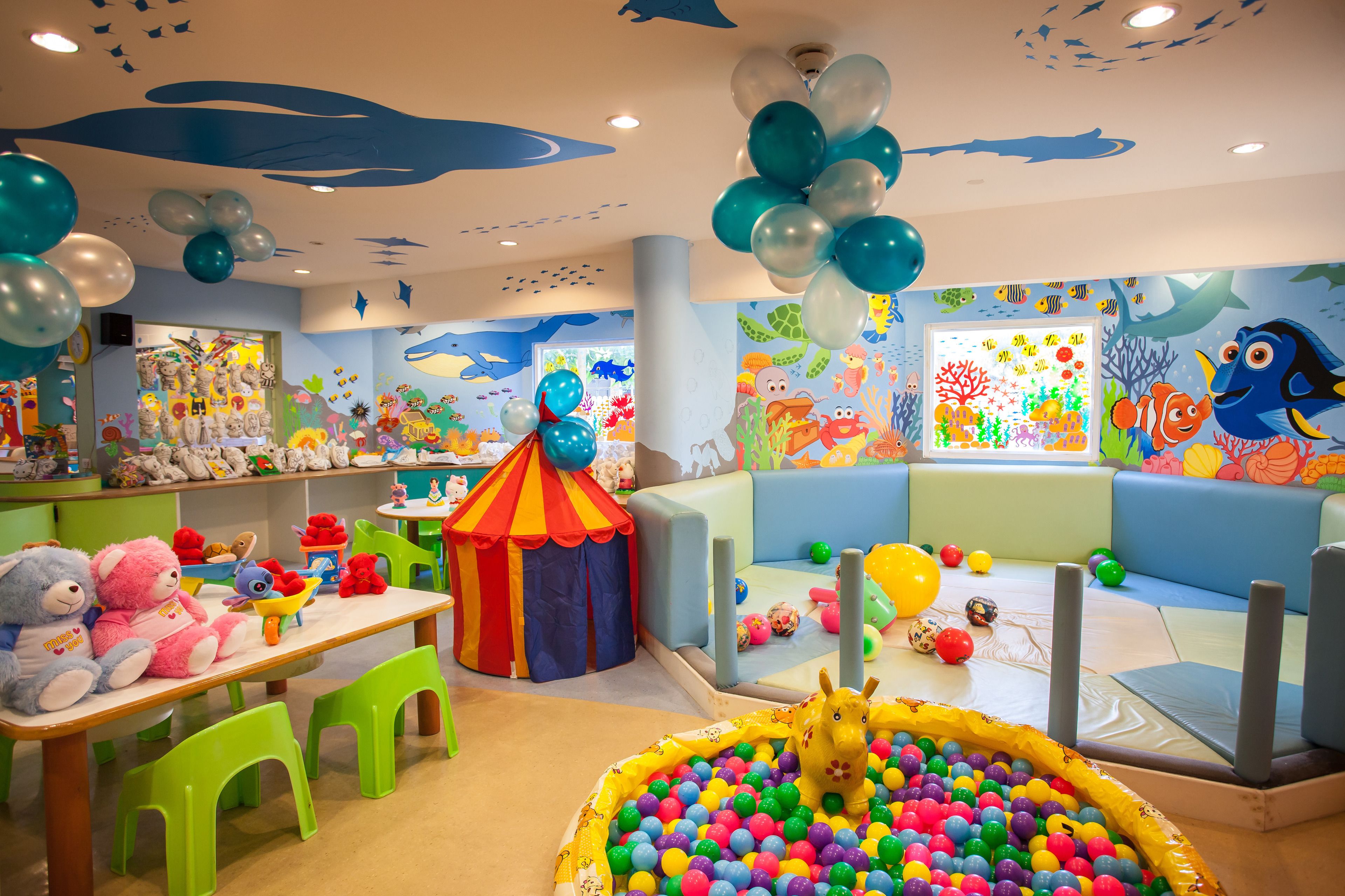 Ein Kinderspielbereich mit Bällebad, Hüpftieren und einer farbenfrohen Wandmalerei.