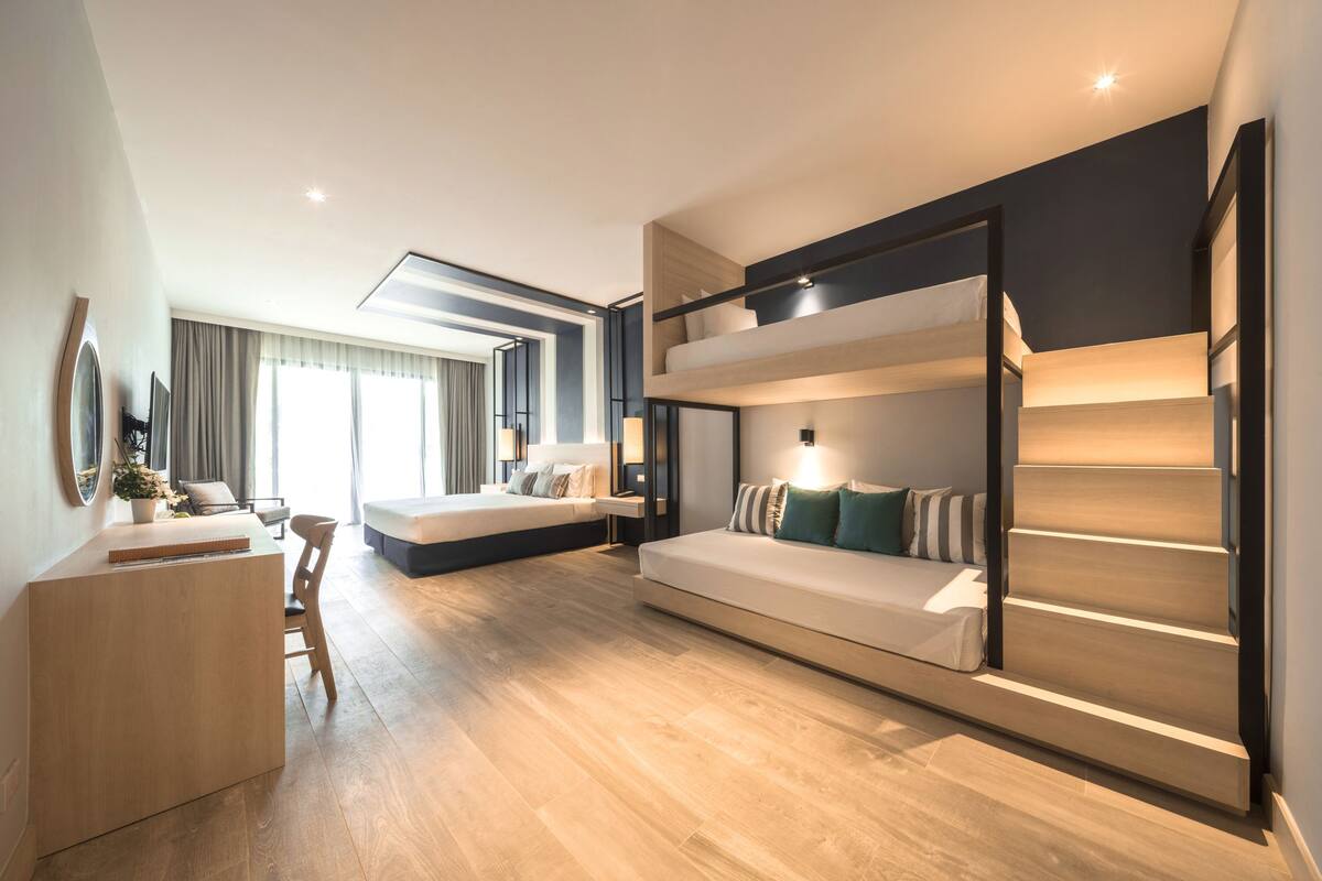 A modern hotel room with a bunk bed, a sofa, a desk, and a large window.