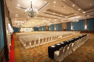 Un amplio salón de conferencias con filas de sillas blancas, una larga mesa con placas de identificación y candelabros.