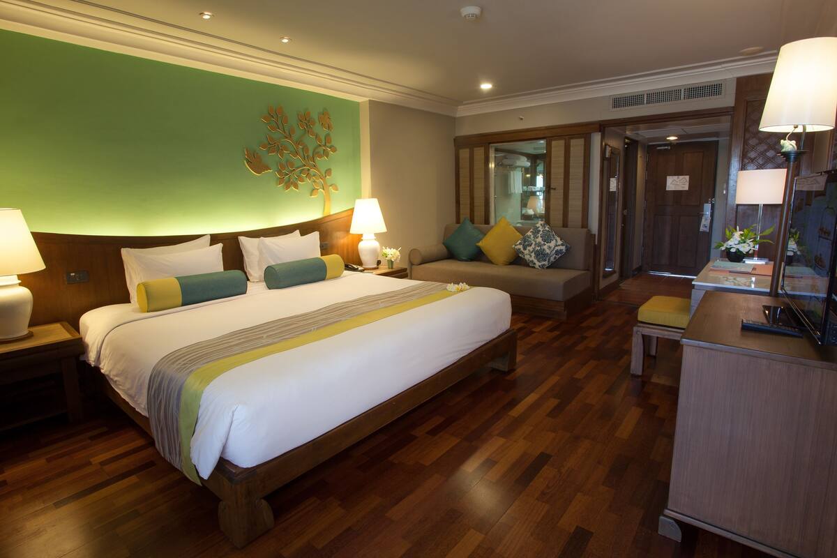 A hotel room with a large bed, two bedside tables with lamps, a sofa, and a small table with a lamp.