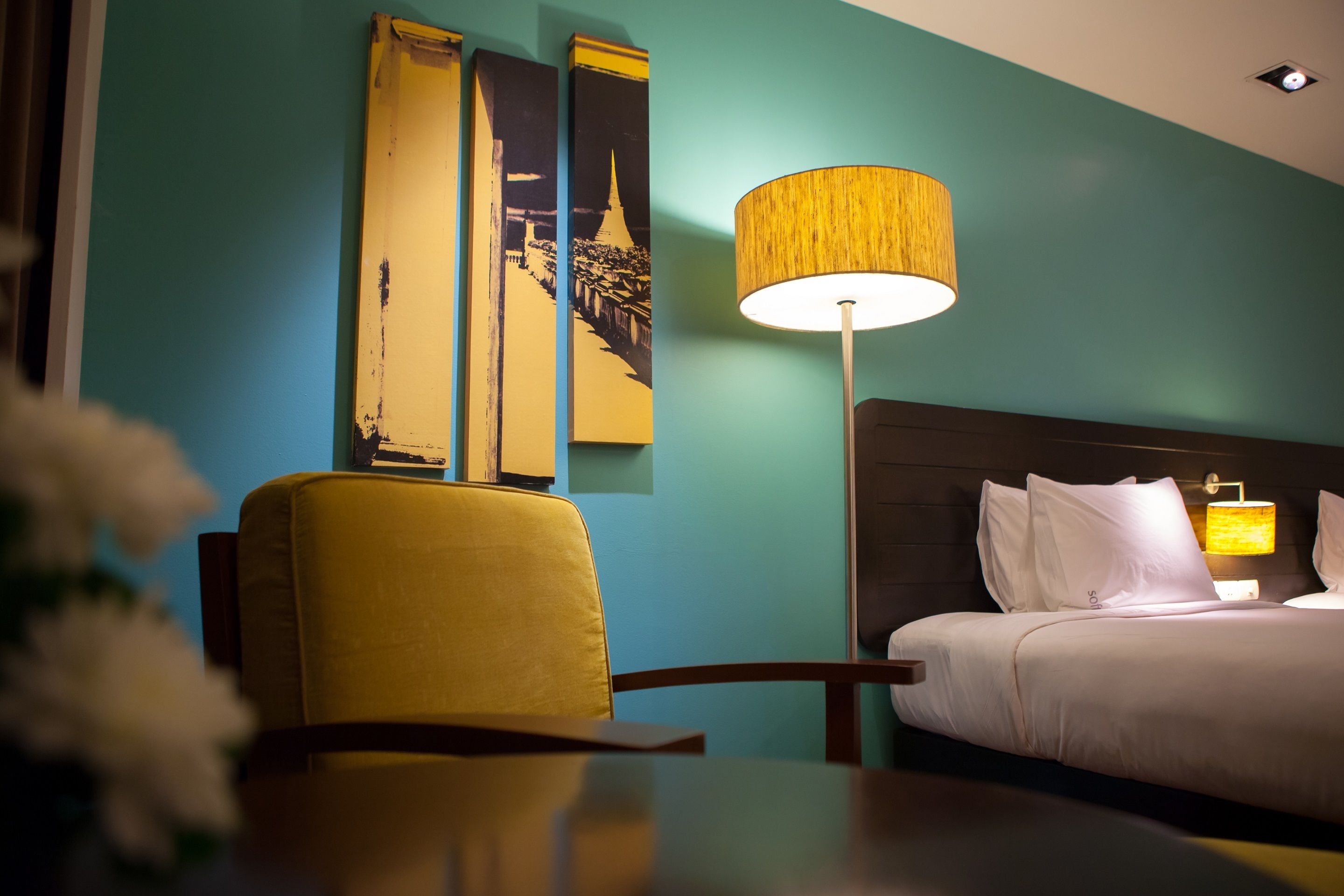 Une chambre d’hôtel équipée d’un lit, d’un bureau, d’une chaise, d’une lampe et d’œuvres d’art murales.