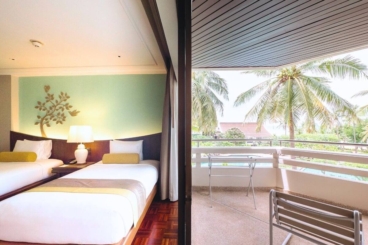 A hotel room with two beds, a nightstand, and a view of palm trees and a pool.