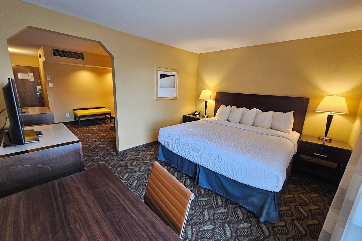 A hotel room with a bed, bedside lamps, a desk with a computer, a chair, and a patterned carpet.