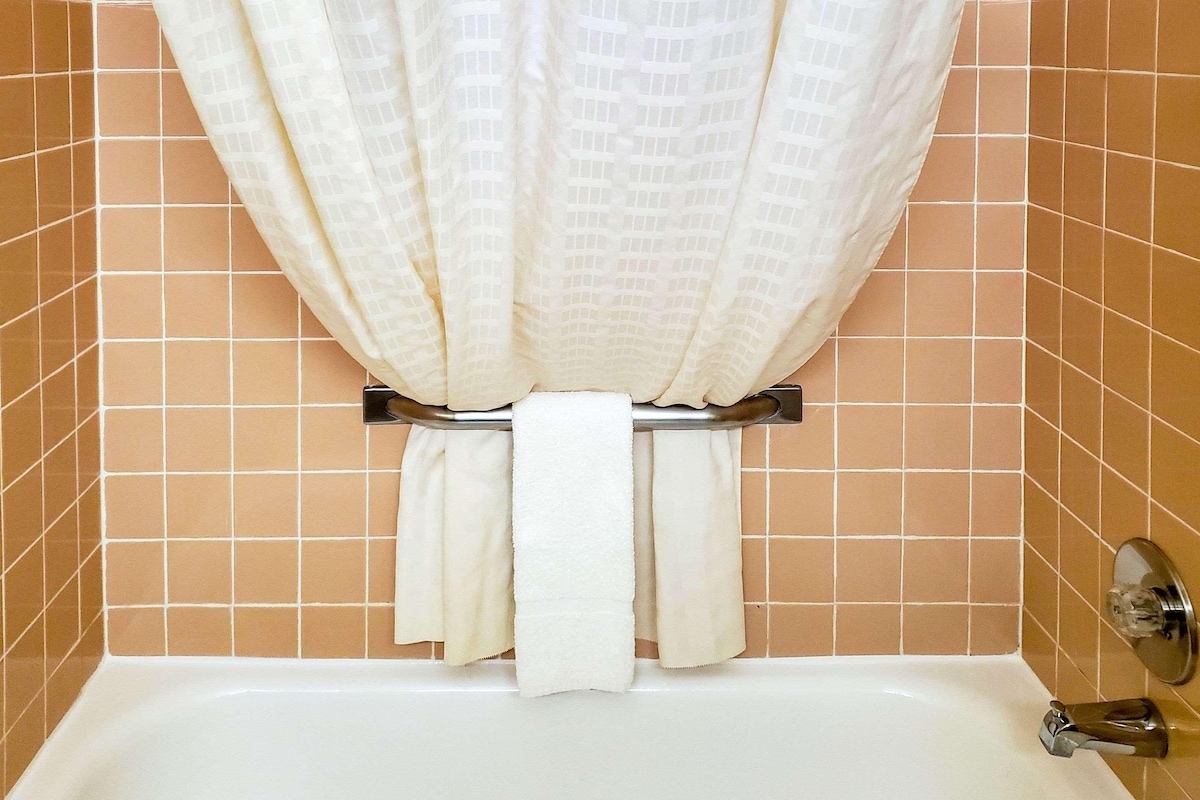 A bathroom with a bathtub, a towel rack with a white towel, and brown tiled walls.