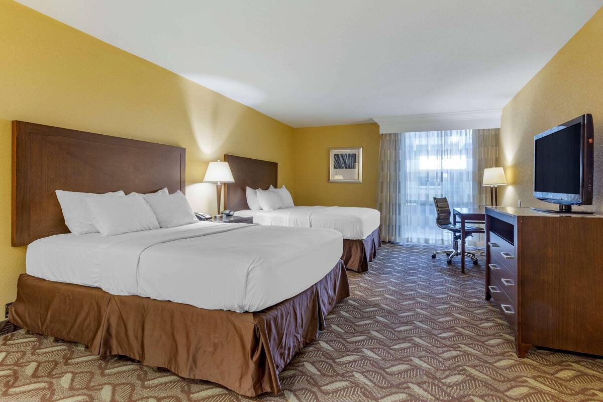 A hotel room with two beds, a desk, a television, and a window with curtains.