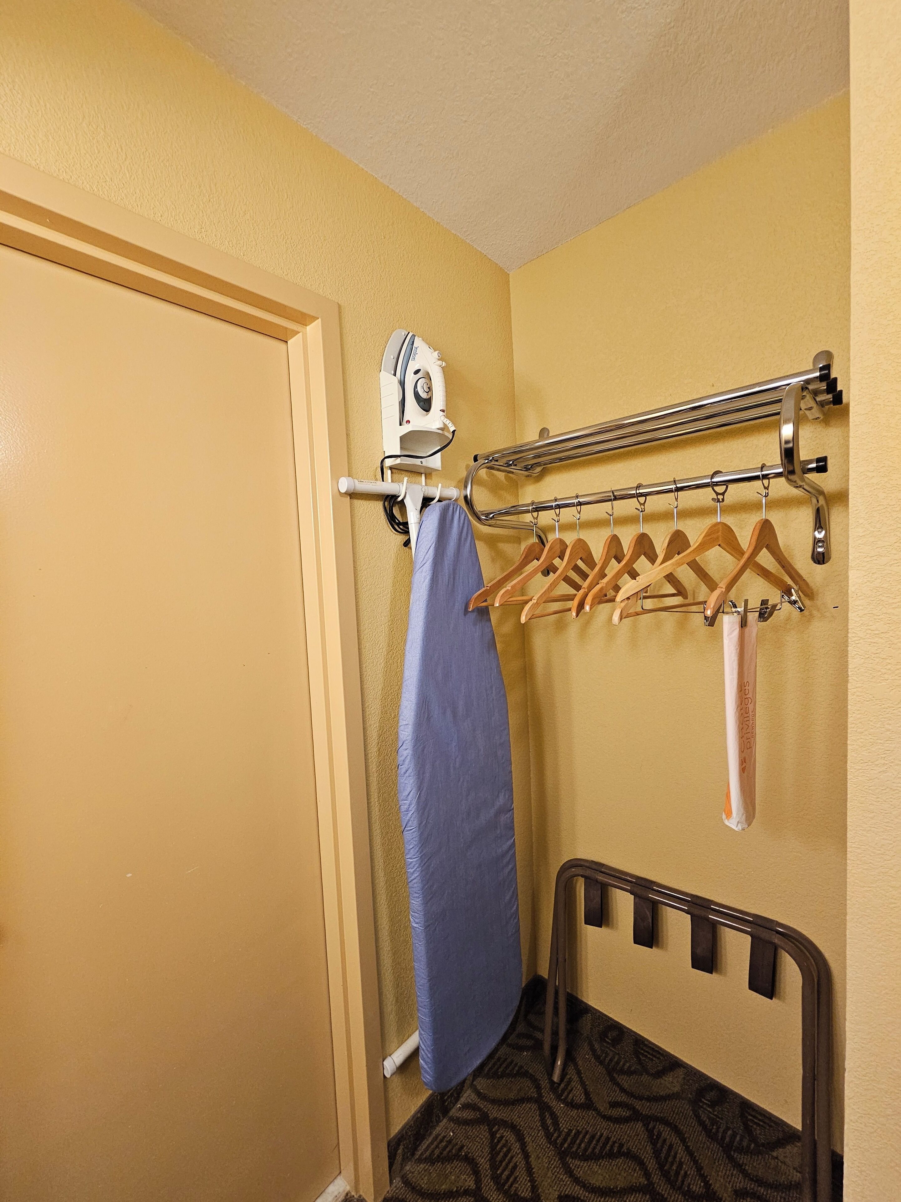 A hotel room with a bed, a towel rack with hangers, and a wall-mounted iron.